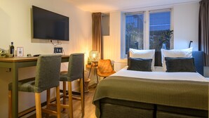 A hotel room with a bed, a desk with two chairs, a TV, and a window with curtains.