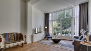 A spacious living room with a large window, a white sofa, a black armchair, and a coffee table.