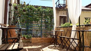 Un patio al aire libre con mesas y sillas de madera, una cerca de bambú y plantas en macetas.