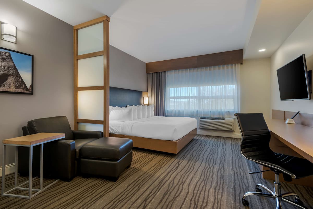 A hotel room with a bed, a desk, a chair, a small table, a TV, and a window with curtains.