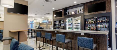 A modern bar area with a counter, bar stools, and a variety of liquor bottles.