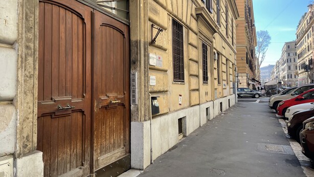 A street with parked cars and a building with large wooden doors and multiple windows.