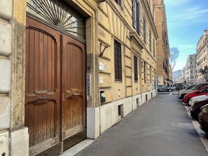 A street with parked cars and a building with large wooden doors and multiple windows. - Roman Holidays Rooms Otranto (Rome)