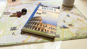 A travel map of Rome with a guidebook, keys, a keychain, and a small plant.