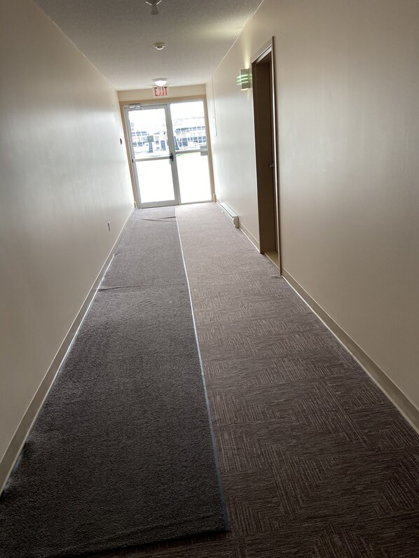 A hallway with carpeted floors, a door on the right, and an exit sign above the door.