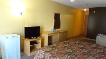 Ein Hotelzimmer mit Bett, Schreibtisch mit Spiegel, Fernseher und Kühlschrank.