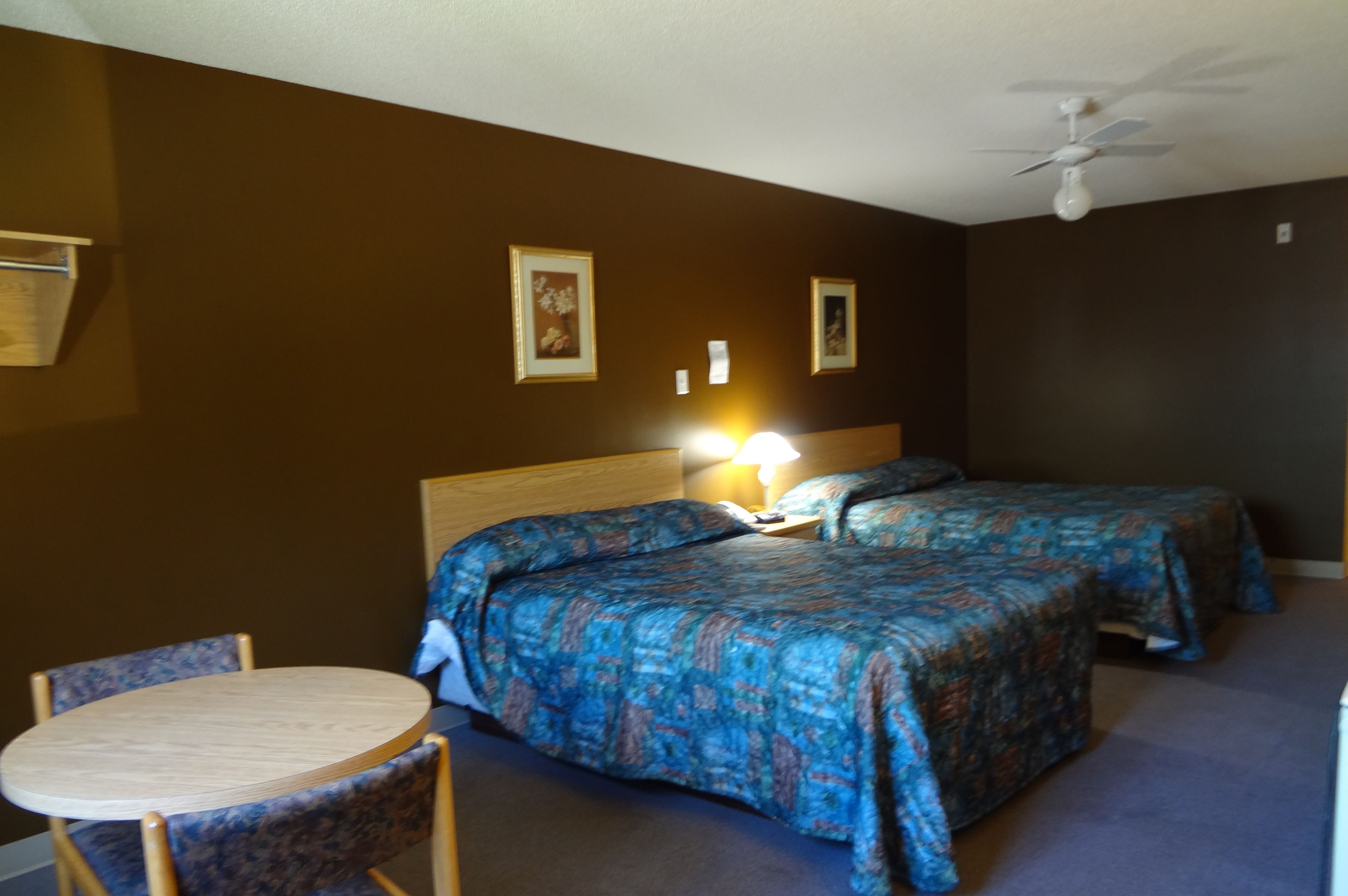 A hotel room with two beds, a round table, and a ceiling fan.