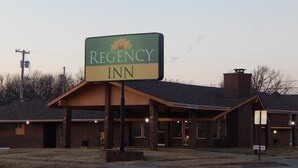 A Regency Inn sign with a flower emblem, a brick building with a flat roof, and a clear sky. - Regency Inn lola Kansas (Iola)