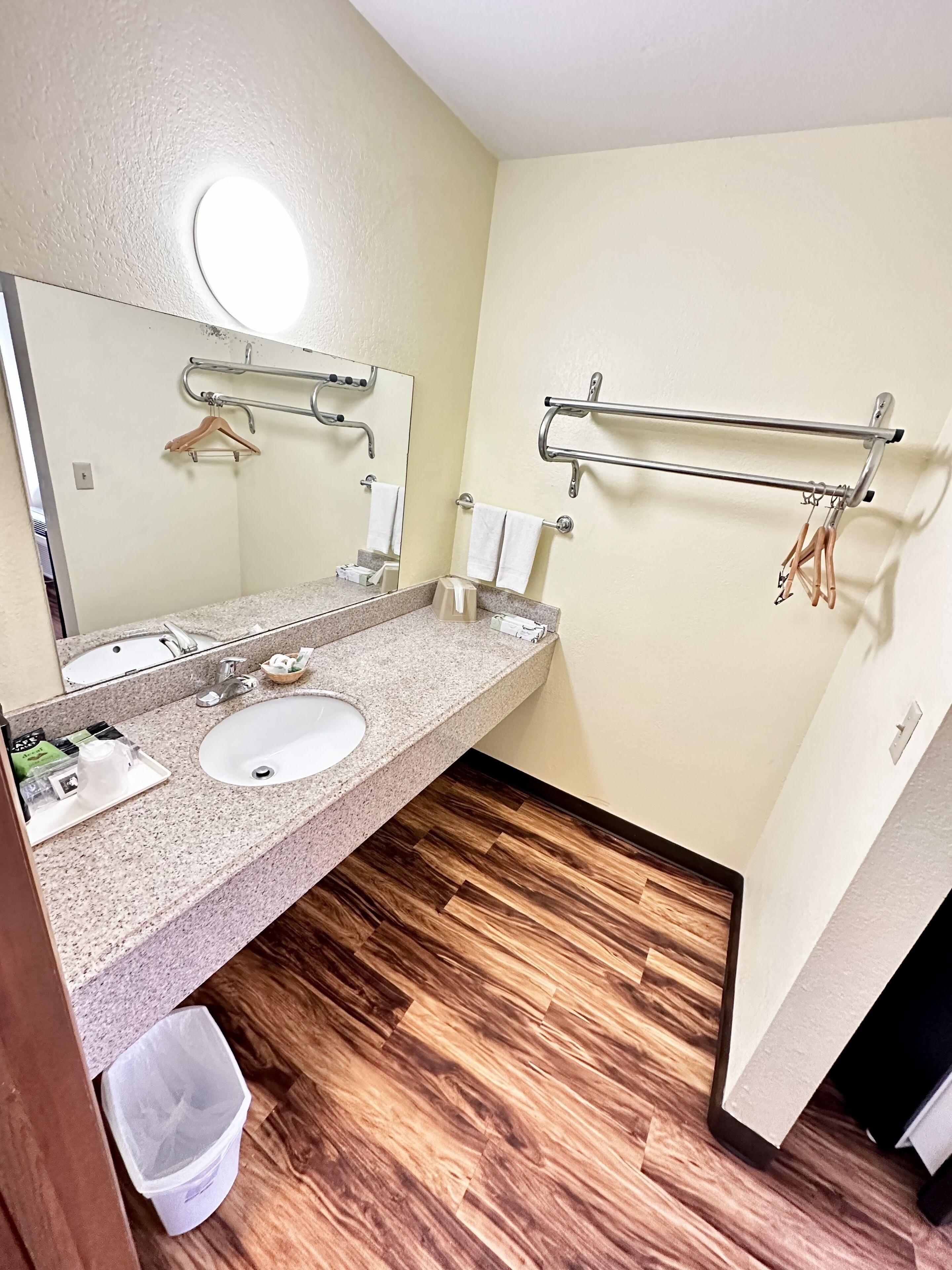 A bathroom with a granite countertop, a sink, a mirror, a towel rack, and a trash bin.
