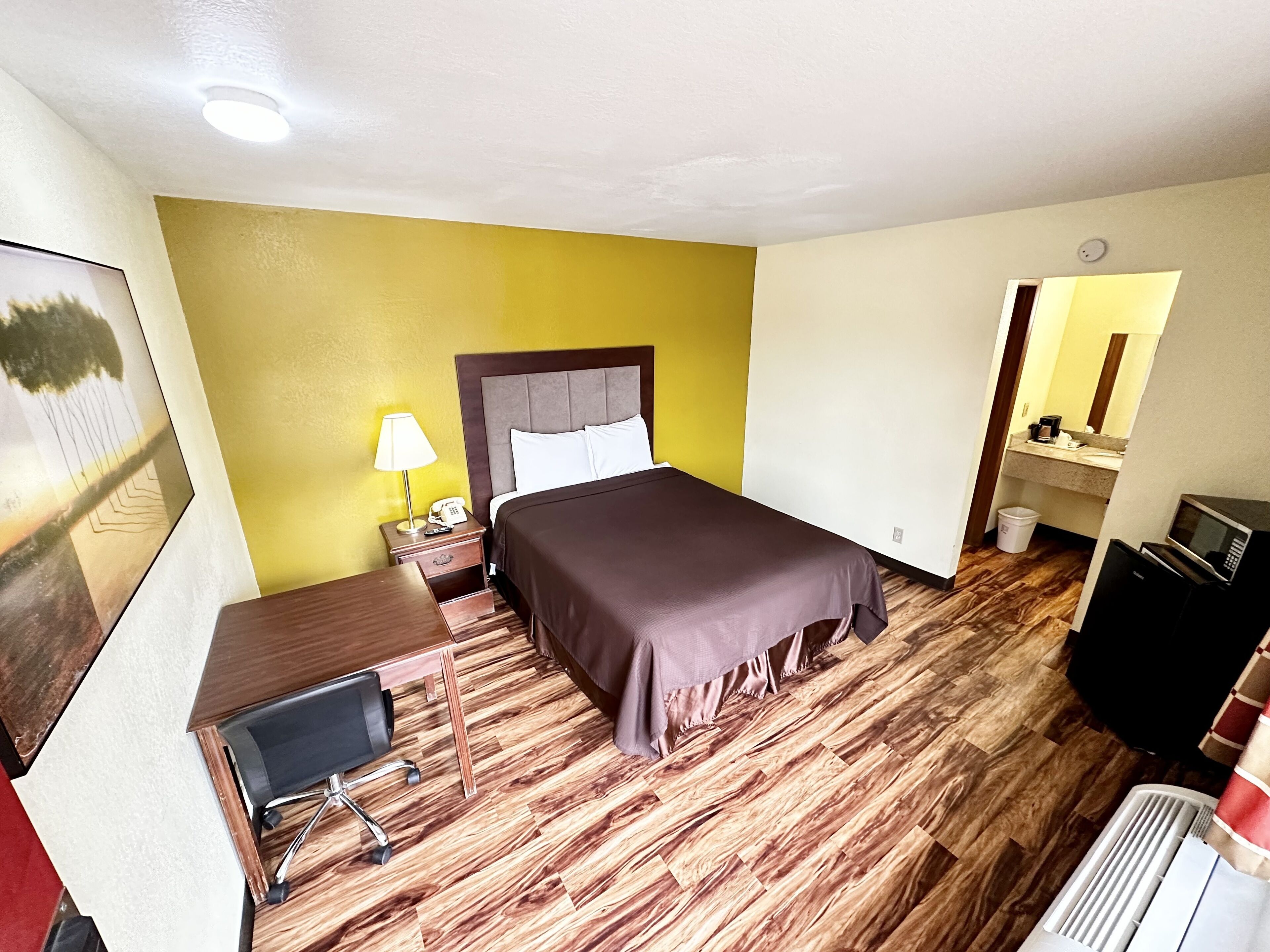 A hotel room with a bed, bedside table, lamp, and a desk with a chair.