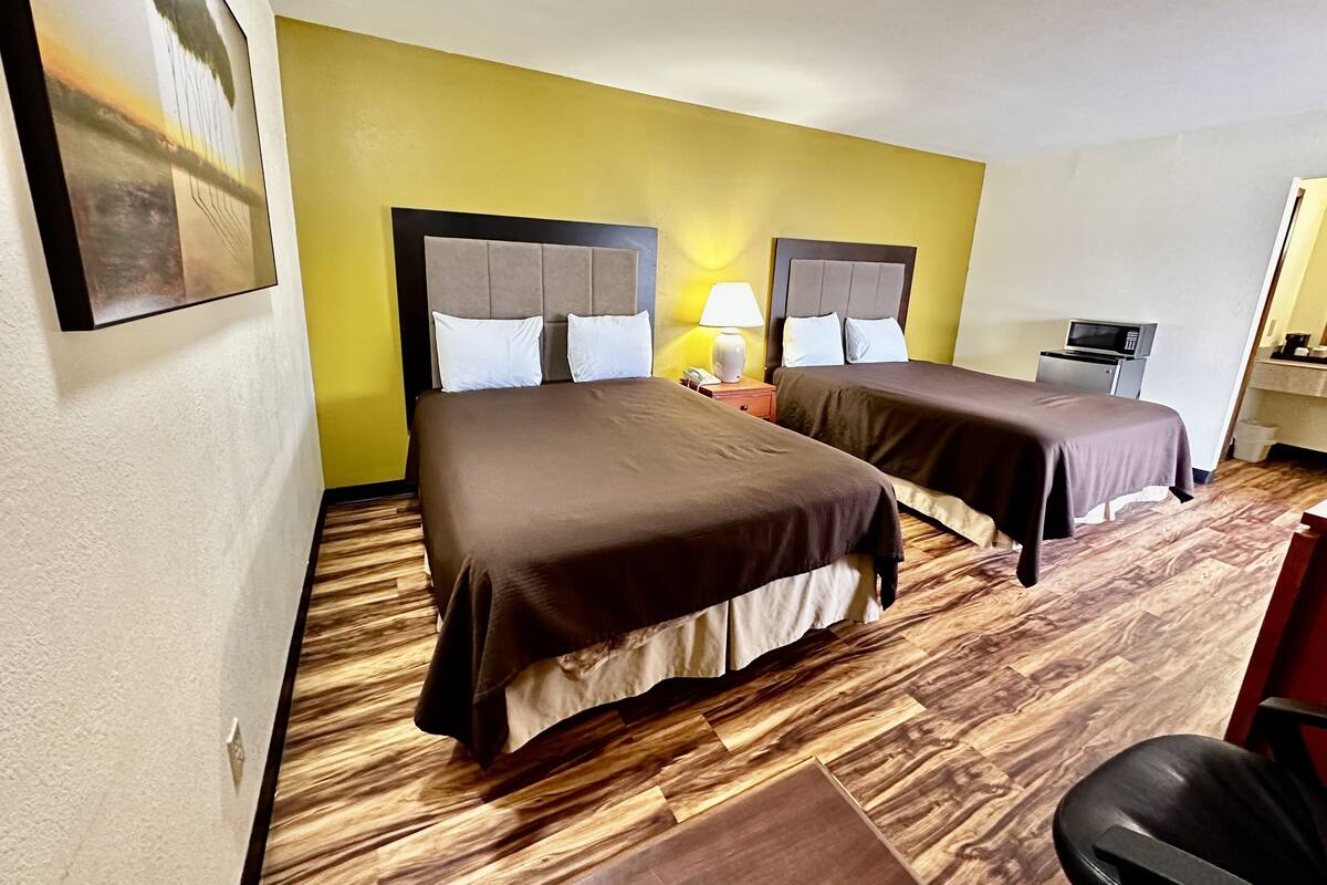 A hotel room with two beds, a desk, a chair, a microwave, and a small kitchenette.