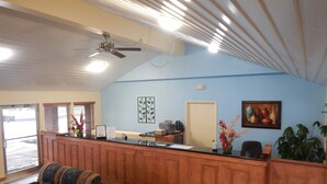 A reception area with a wooden counter, two upholstered chairs, a ceiling fan, and a door. - Regency Inn lola Kansas (Iola)