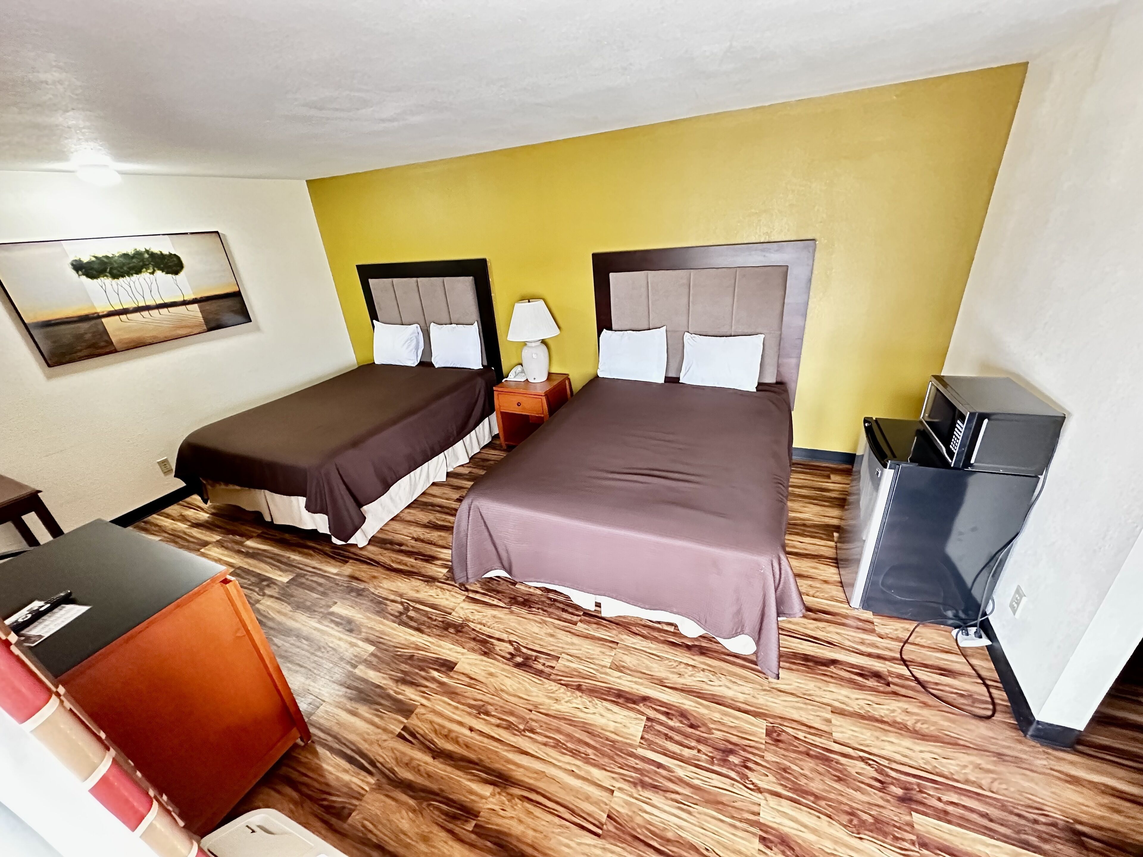 A hotel room with two beds, a desk, a chair, a TV, and a painting on the wall.