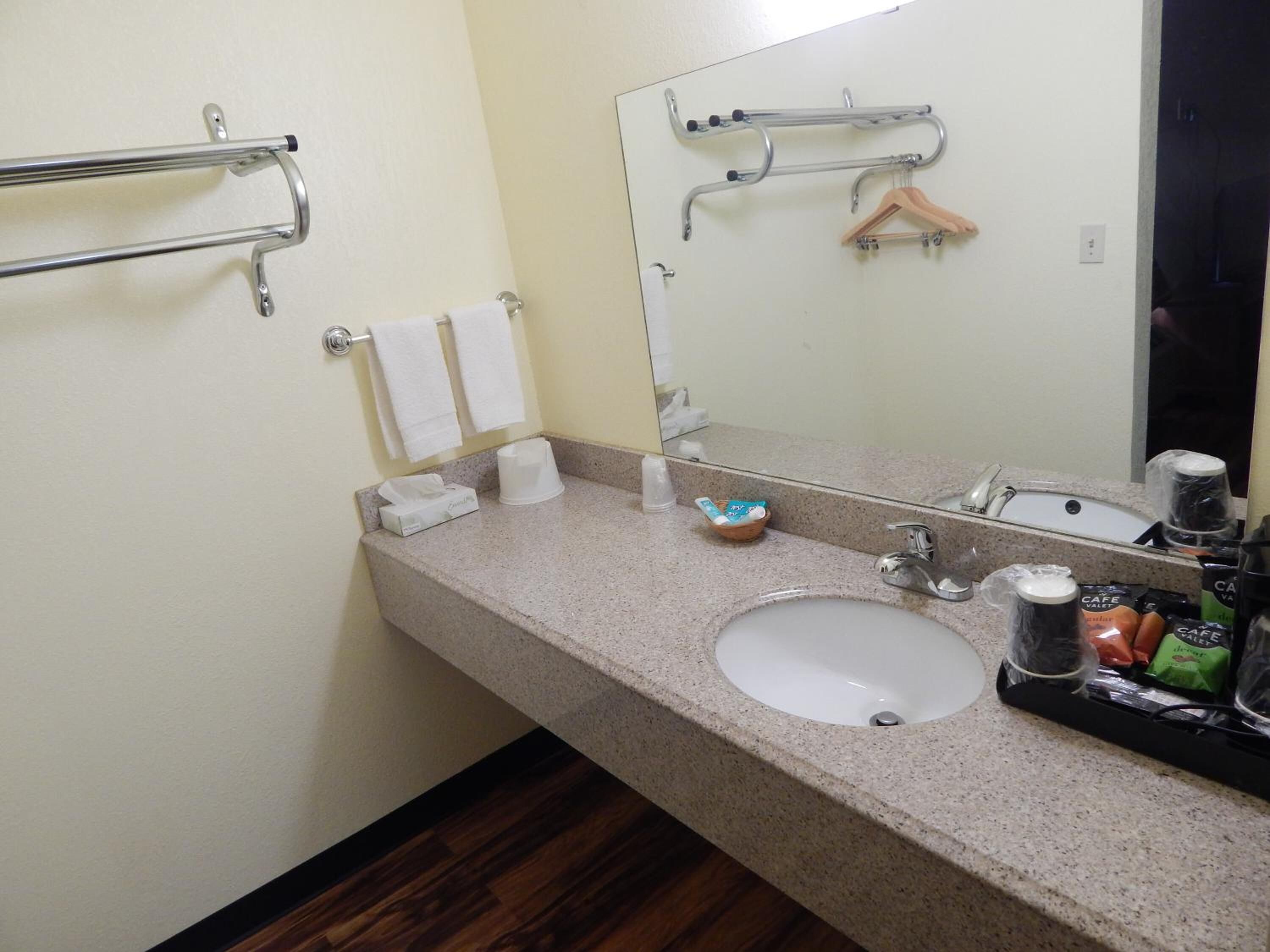 A bathroom with a sink, mirror, towel rack, and toiletries.