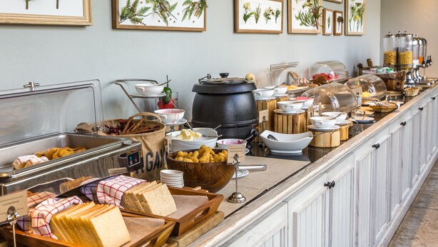 A buffet with various food items, including bread, fruits, and a large black pot. - Regency Inn lola Kansas (Iola)