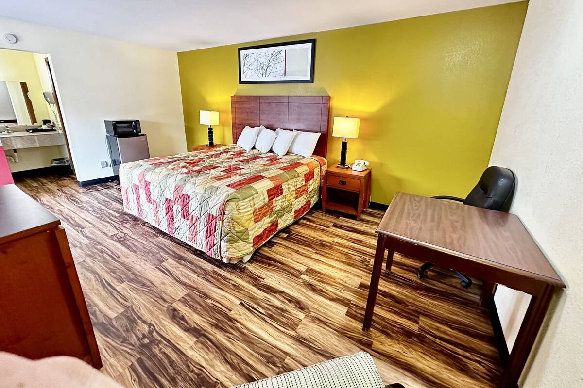 A hotel room with a bed, bedside tables, a desk, and a chair.