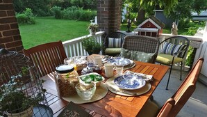 Una mesa de madera dispuesta para una comida, con diferentes platos, un libro y una jaula de pájaros con plantas.
