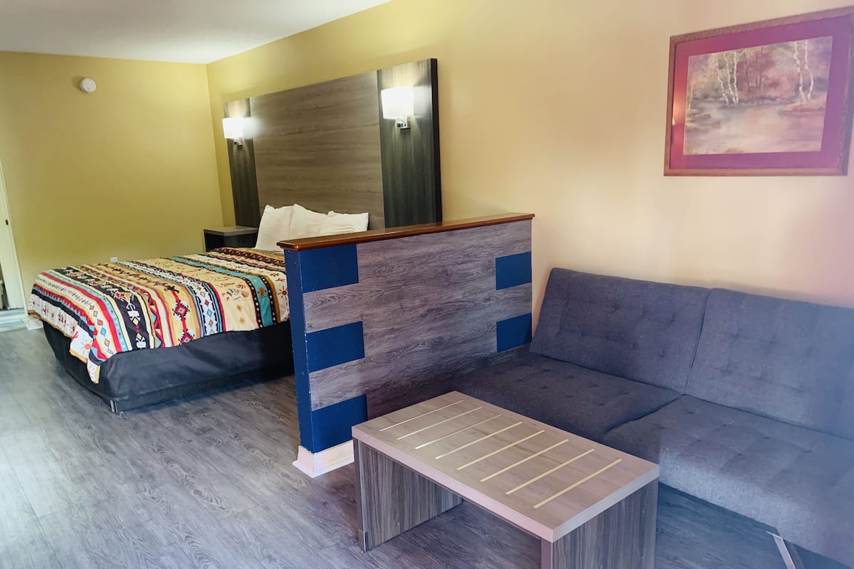 A hotel room with a bed, a sofa, a small table, and a headboard with a wooden finish.
