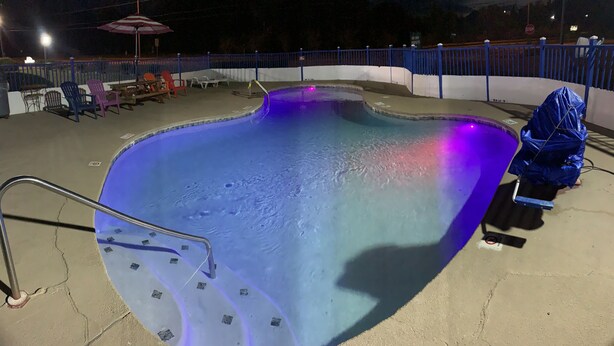 A swimming pool with a blue and purple light, a metal ladder, and a blue fence.