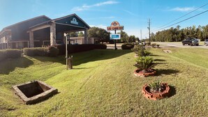 A motel with a covered parking area, a signboard, and well-maintained lawn with potted plants.