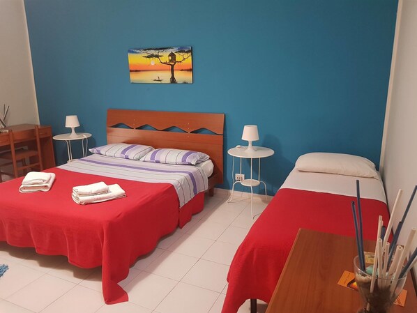 A hotel room with two beds, a wooden headboard, a painting of a sunset, and a small table with a lamp.
