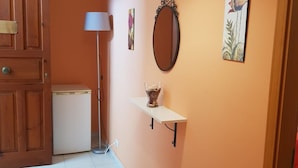 A hallway with a wooden door, a small refrigerator, a floor lamp, a mirror, and a shelf with a vase. - The Artists (Acireale)