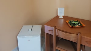 A small room with a wooden desk, a white refrigerator, and a plate of vegetables on the desk. - The Artists (Acireale)