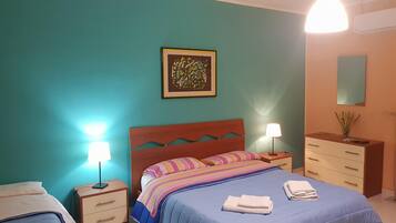 Un dormitorio con paredes verde azulado, una cama de madera con una manta a rayas de colores, dos mesitas de noche con lámparas, un pequeño aparador y una obra de arte enmarcada en la pared.