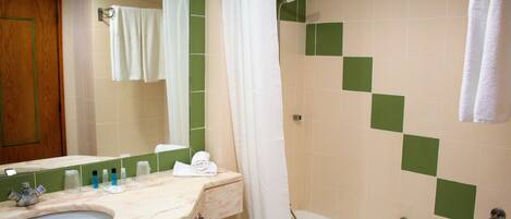 A bathroom with a sink, mirror, shower, and green-tiled walls.