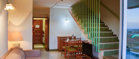 Una sala de estar con un sofá, una mesa de centro, un televisor y una escalera con barandas verdes.