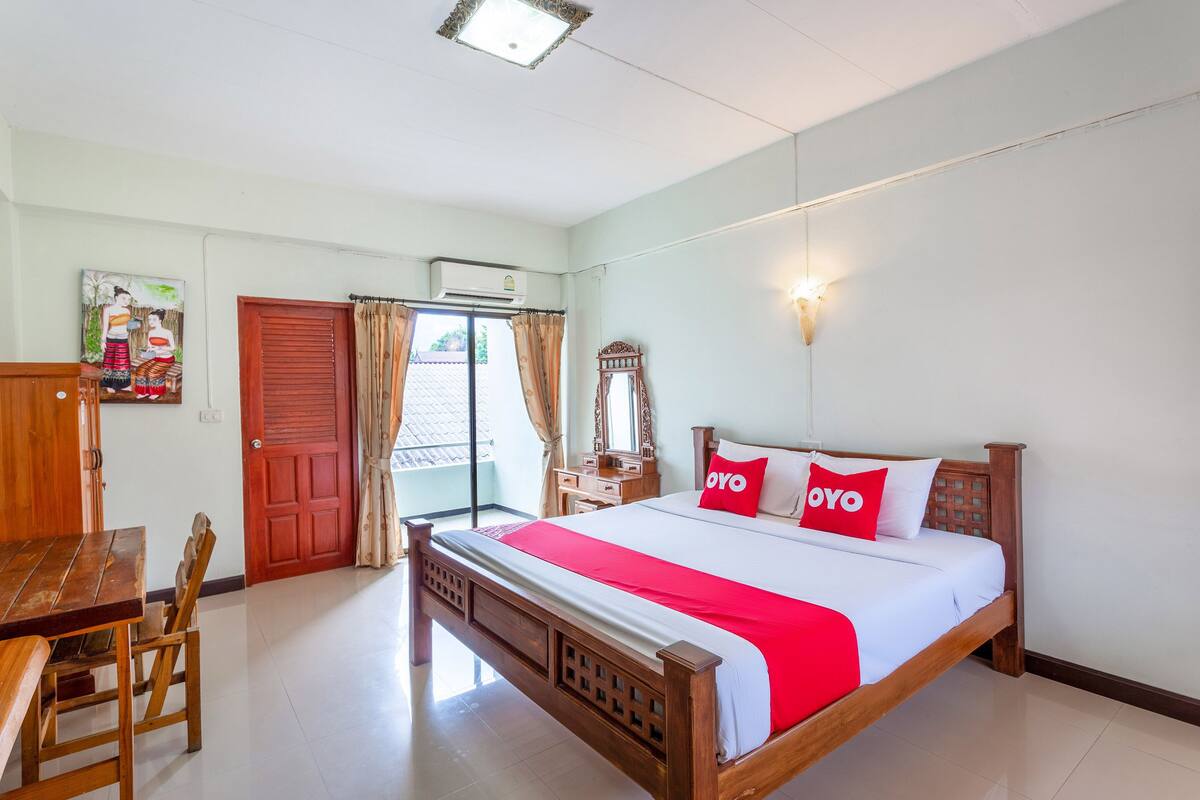 A hotel room with a wooden bed, a red and white bedspread, a wooden desk, and a painting on the wall.