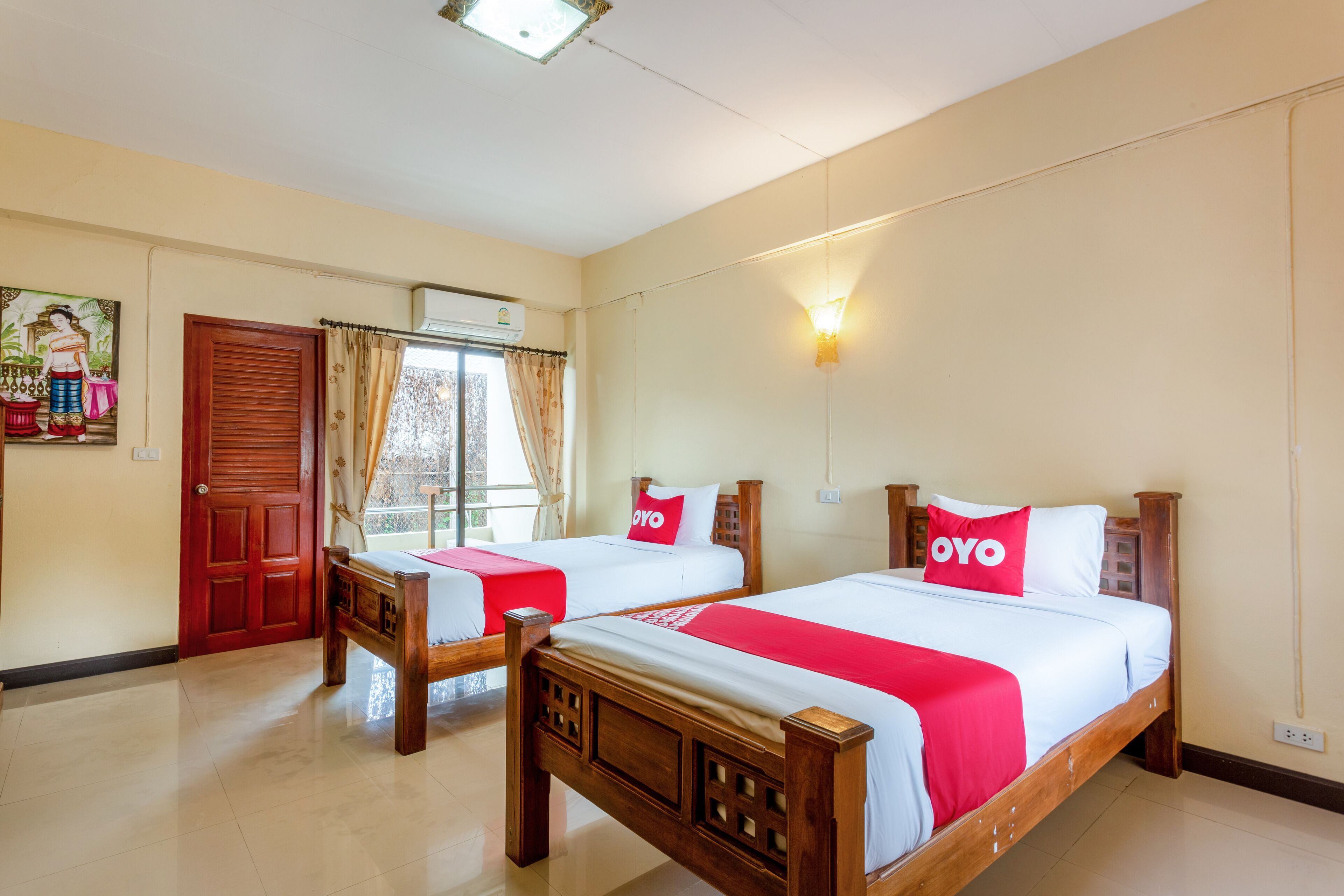 Habitación de hotel con dos camas de madera, cada una con una colcha roja y blanca y almohadas con la palabra 'OYO'.