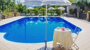 Una piscina con sombrilla blanca, sillas de descanso y una mesa con una bebida.