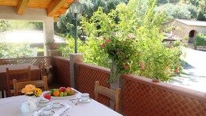 Un área de comedor al aire libre con una mesa preparada para dos personas, rodeada por un muro de ladrillo y plantas en macetas.