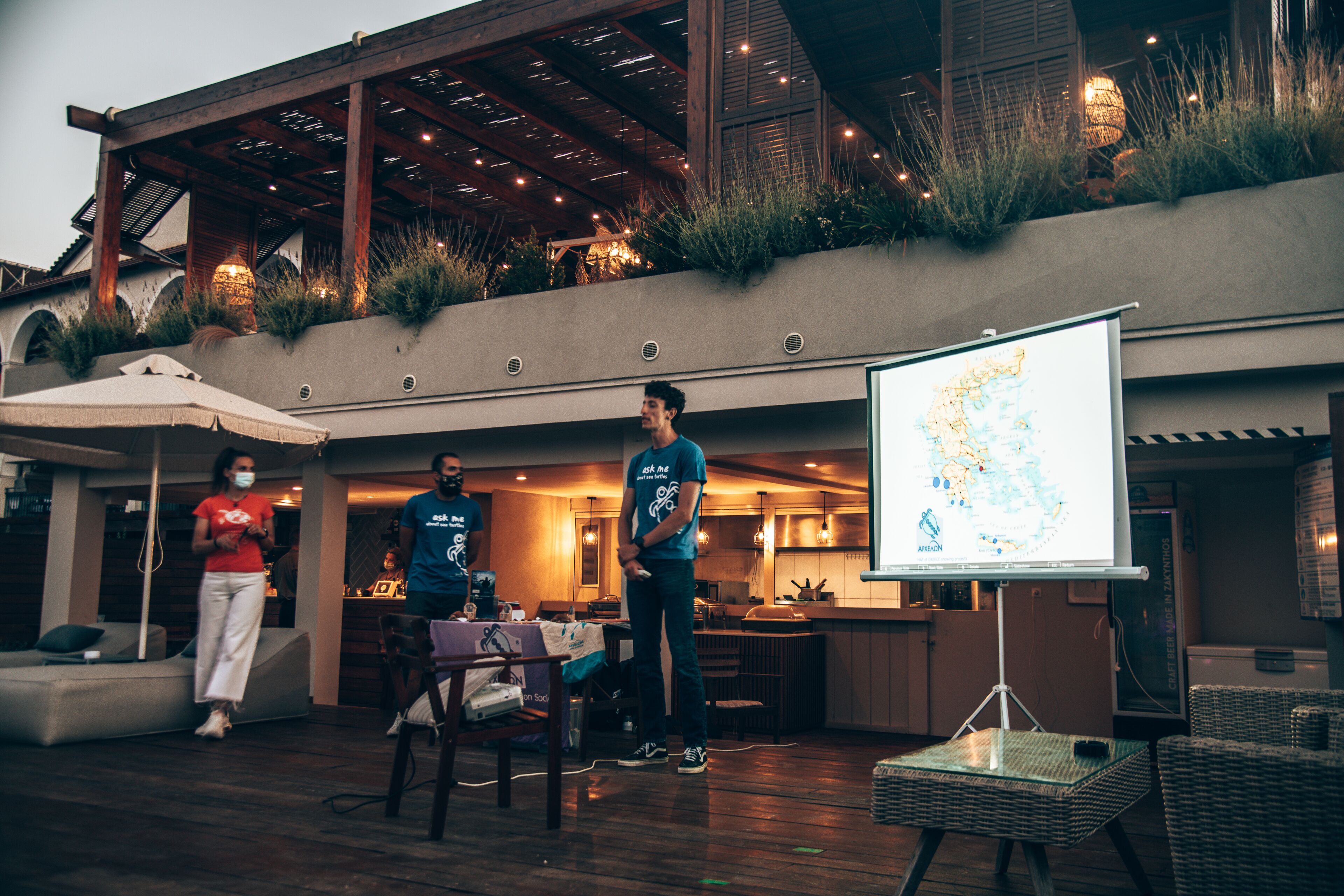 An outdoor patio with a wooden deck, seating area, and a large screen displaying a map.