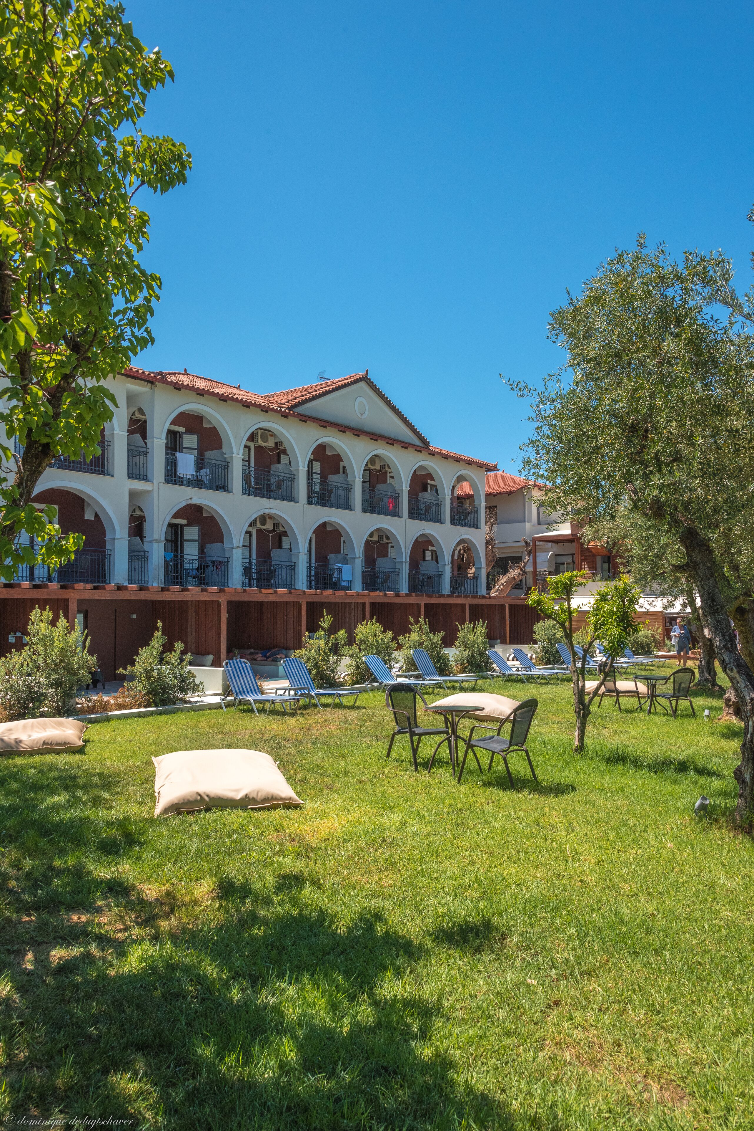 A hotel with a courtyard featuring sun loungers, a pool, and a large building with multiple balconies.