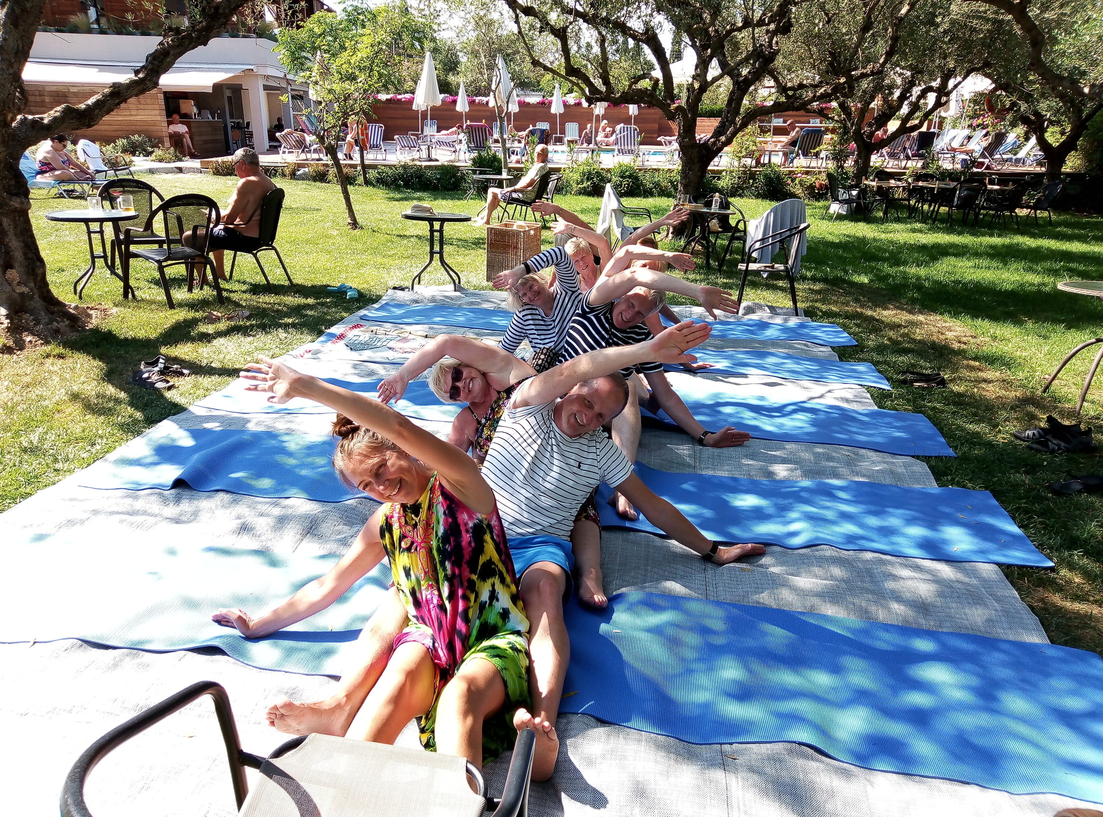 Un grupo de personas sobre esterillas de yoga al aire libre, con una piscina y sillones de descanso al fondo.