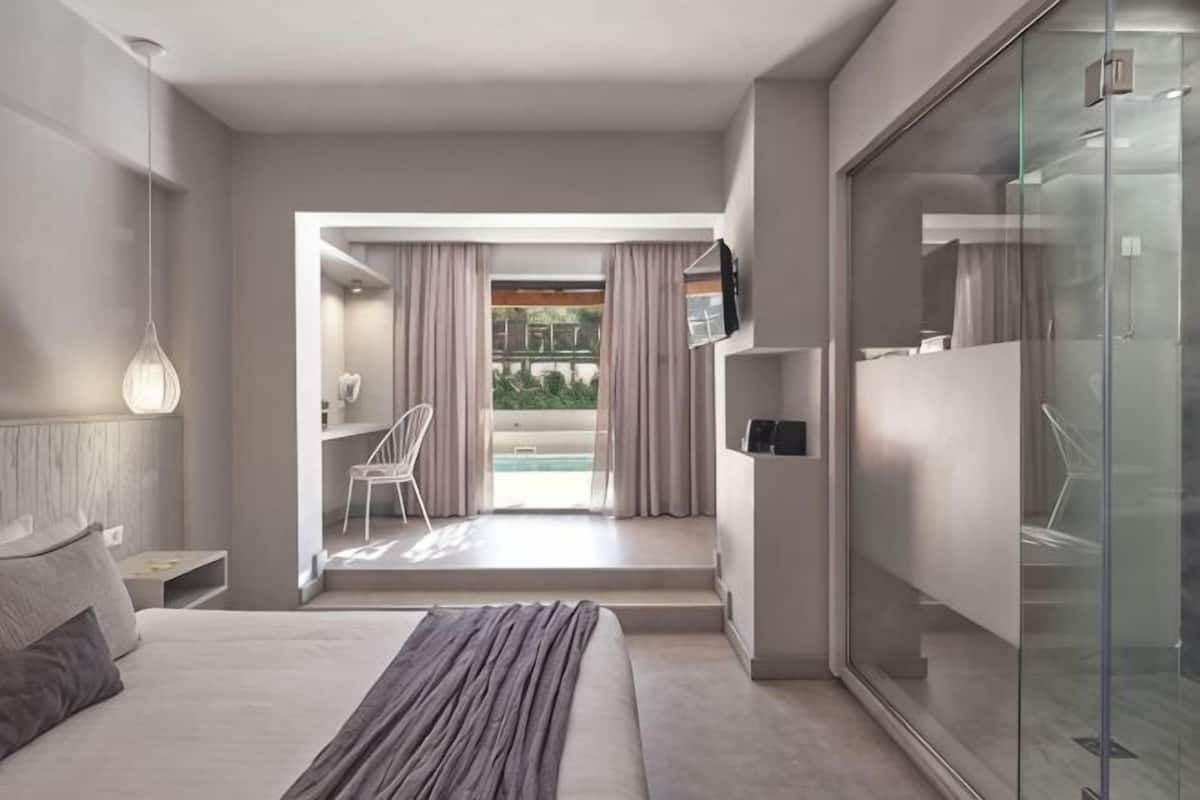 Camera d'albergo moderna con un letto, un divisorio in vetro, una scrivania con una sedia e vista all'esterno.