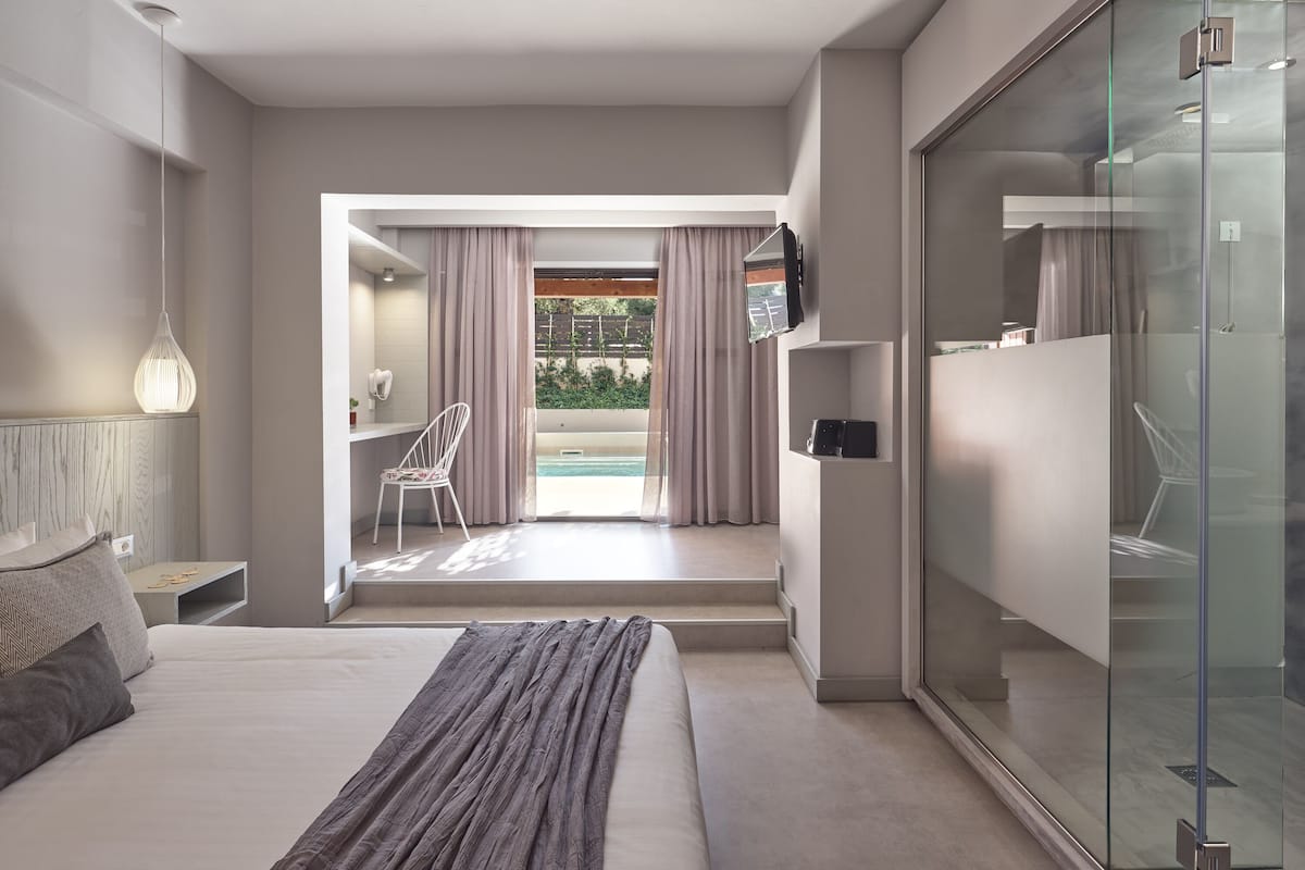 Camera d'hotel moderna con un grande letto, cabina doccia in vetro, TV a parete e vista su una zona piscina.