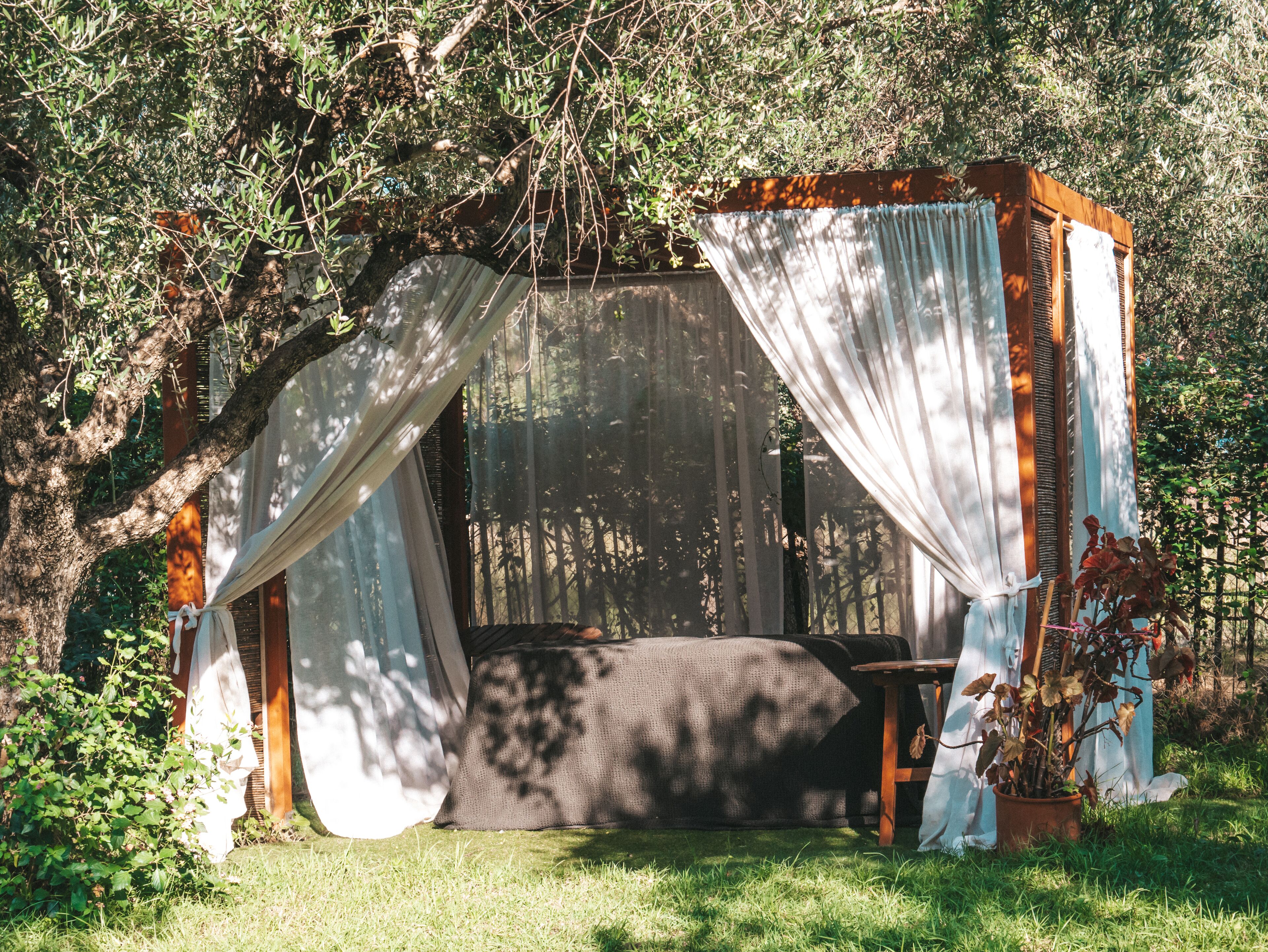 A secluded garden with a rustic wooden gazebo, a comfortable seating area, and lush greenery.