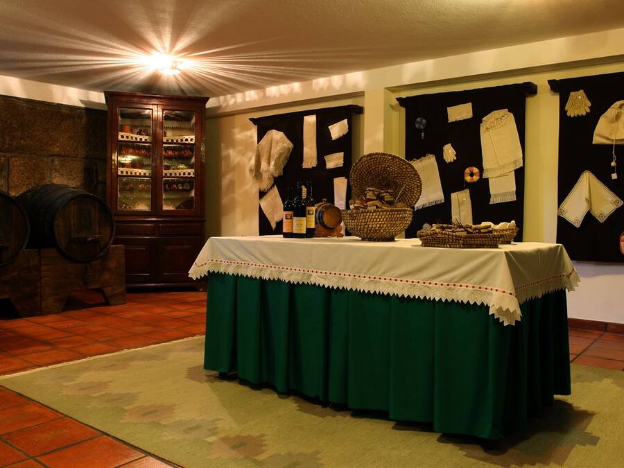 A room with a table covered in a green tablecloth, a wooden cabinet with glass doors, and a display of textiles on the wall.