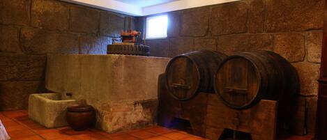 Una habitación con paredes de piedra, una ventana, un barril de madera, un bloque de hormigón y un suelo de baldosas.