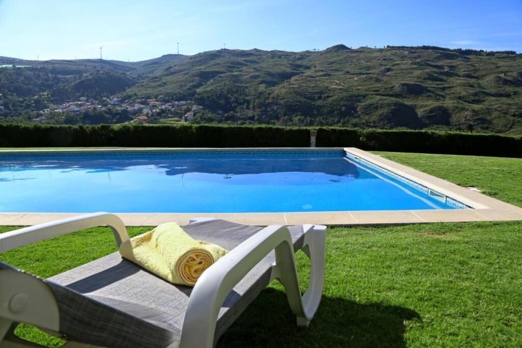 A swimming pool with a view of green hills and a chair with a towel.