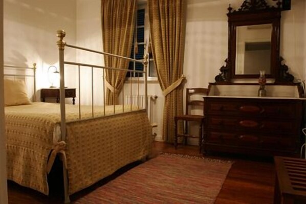 A traditional bedroom with a four-poster bed, a dresser, a mirror, and a window with curtains.