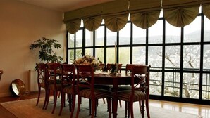 Un coin repas avec une grande fenêtre, une table à manger, des chaises, une plante et une horloge posée sur le sol.