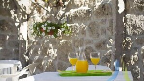 Une table dressée à l’extérieur, avec un mur de pierres en arrière-plan, un set de table vert et deux verres de jus d’orange.