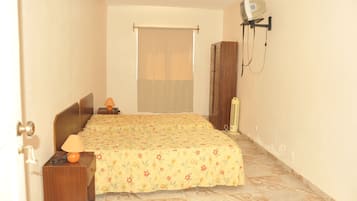 Una habitación pequeña y estrecha con una cama, una mesita de noche, una lámpara y un calentador fijado a la pared.