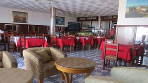 Een restaurant met ronde tafels en stoelen, rode tafelkleden en een betegelde vloer.