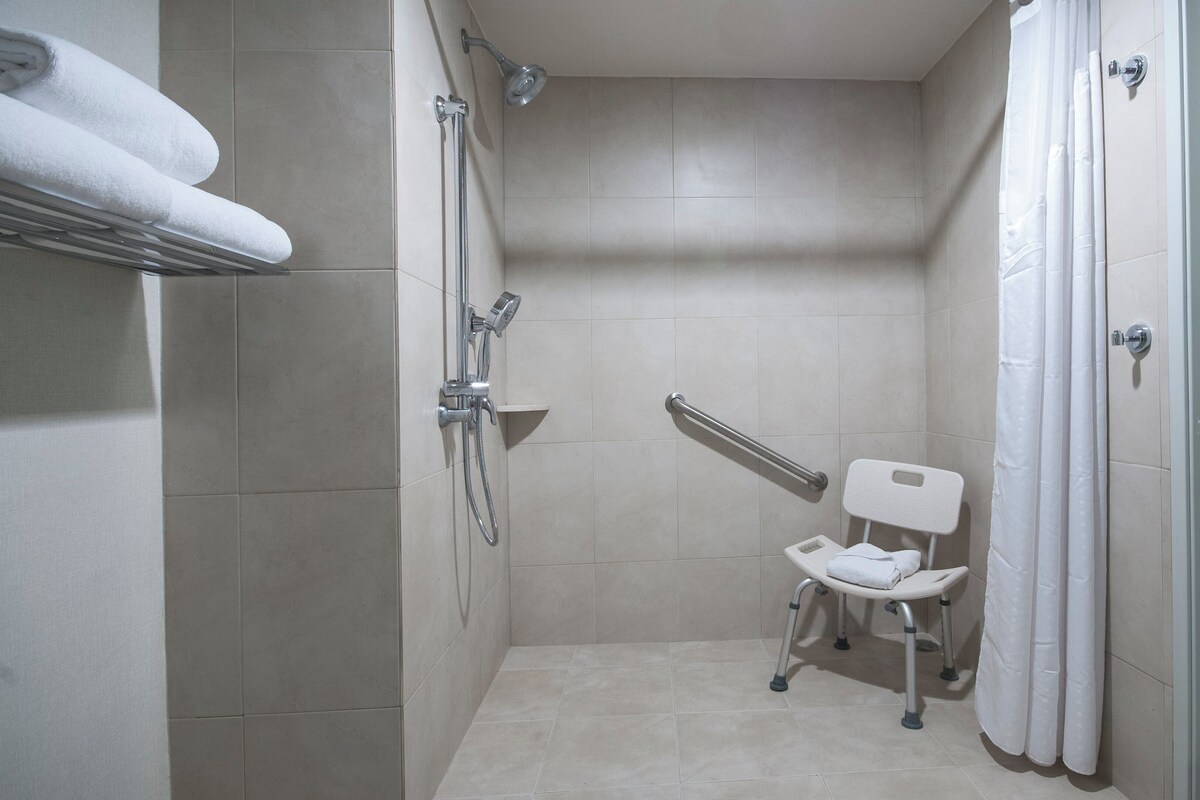 Une petite salle de bain carrelée, équipée d’une douche, de toilettes et d’une barre d’appui.