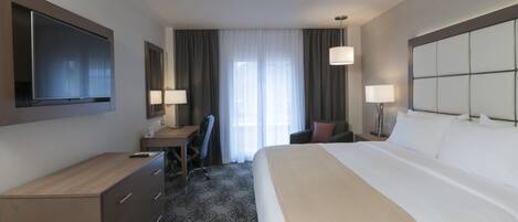 A hotel room with a bed, desk, chair, and a TV mounted on the wall.